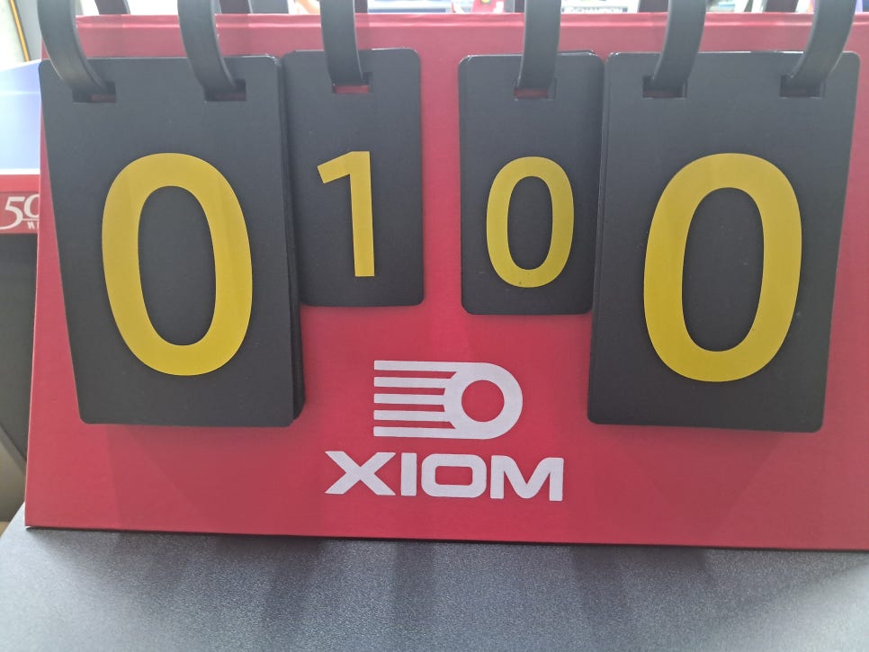 빨간 XIOM 점수판에 바깥쪽 큰 숫자는 양쪽 모두 0, 안쪽 작은 숫자는 왼쪽 1과 오른쪽 0으로 표시되어 있다